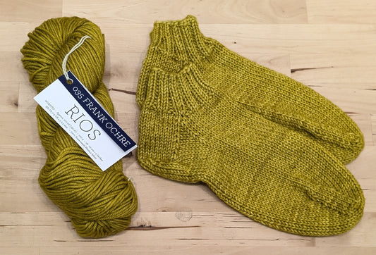 A pair of yellow knitted socks displayed next to a skein of Malabrigo Rios yarn.